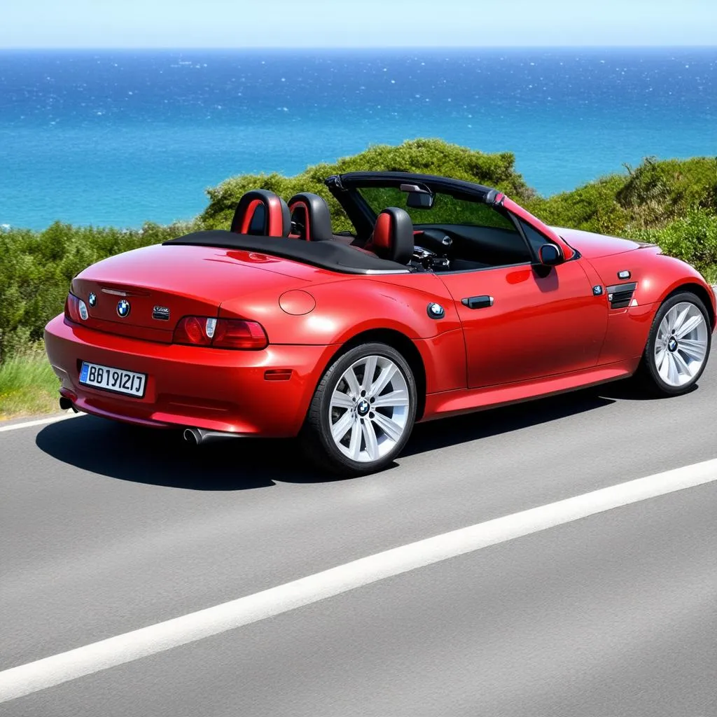 A red 2002 BMW M roadster parked on a coastal highway overlooking the ocean.