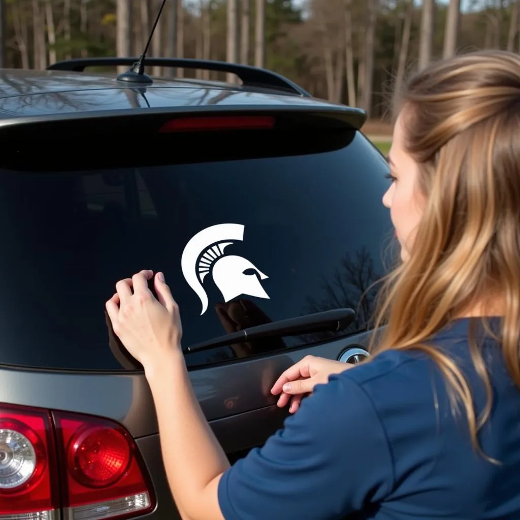 Person applying a Michigan State car decal on their car's back window