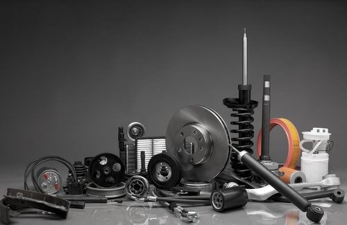 Customers discussing car parts with a mechanic in an auto repair shop, considering whether to supply their own parts for installation.