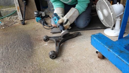 Using a wire brush drill attachment to remove rust from a repurposed car suspension arm.