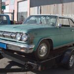 A worn down, teal-colored car sits on a car tow.