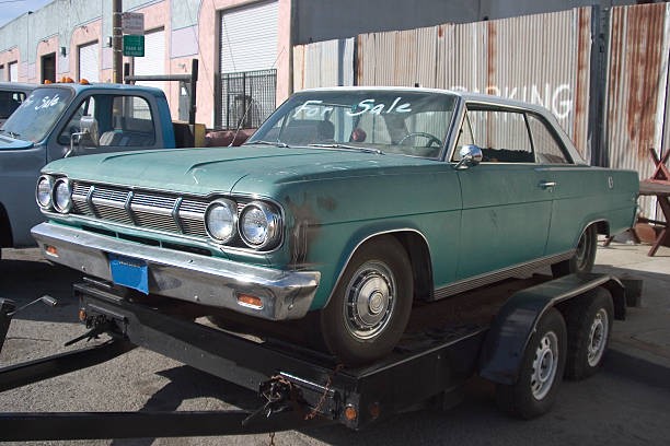 Worn teal car on tow truck for selling car parts for cash