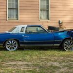 A beaten up junk car sitting on the side of a house.