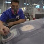 Close-up of a technician's hands grinding down a plastic car part, preparing it for repair.