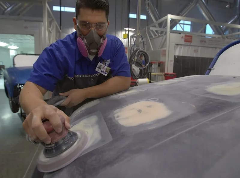 Close-up of a technician's hands grinding down a plastic car part, preparing it for repair.