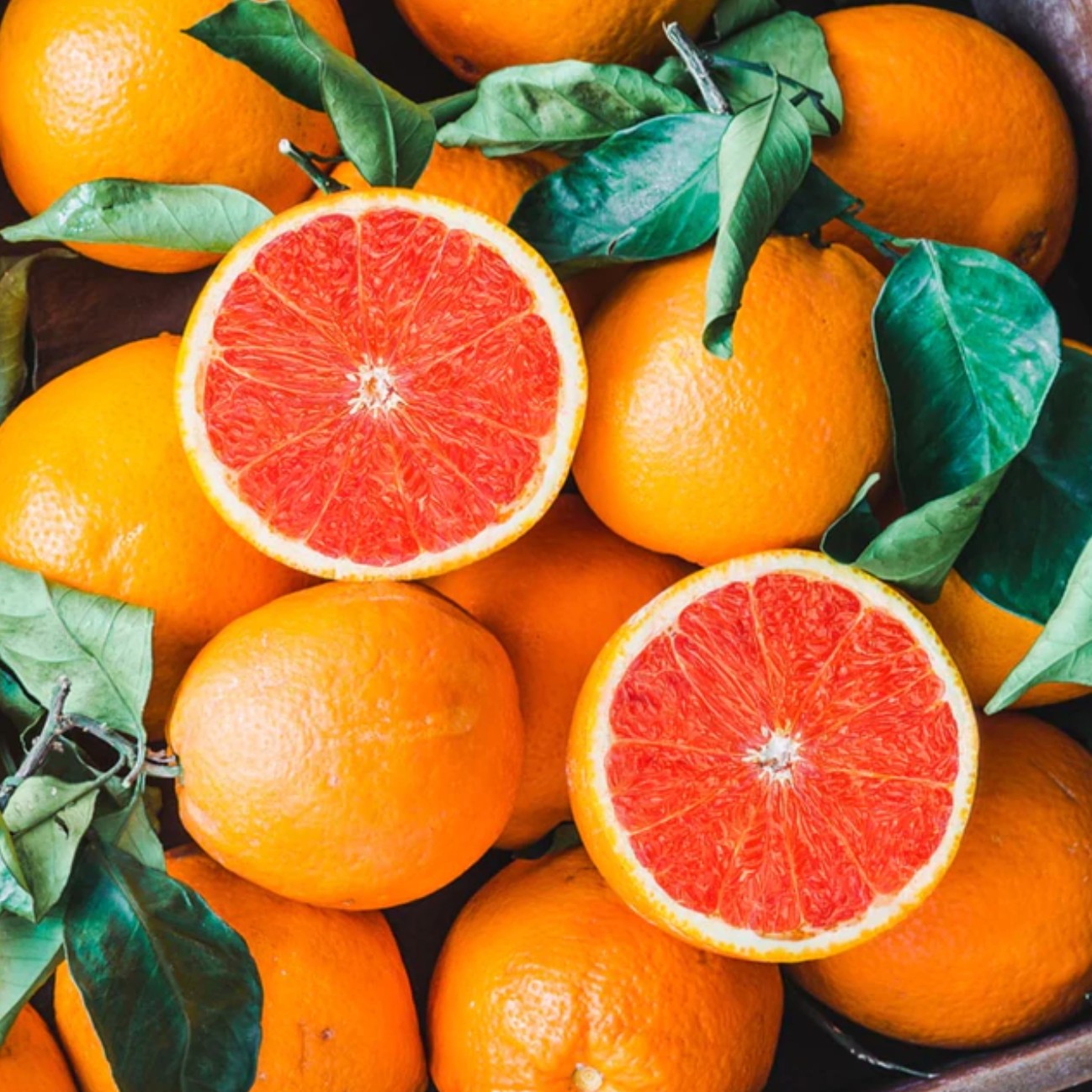 Close-up view of halved Cara Cara oranges showcasing their distinctive pinkish-red flesh alongside whole oranges and leaves.